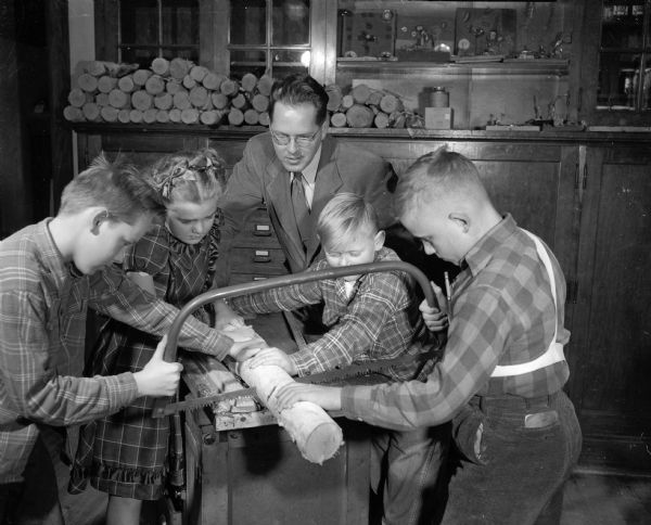 Sixth grade teacher Don Reppen of Emerson School oversees students as they cut a log to be used in making lamps. The students, left to right, are: Don Spring, Mary Ellen Edland, Jimmy Nelson, and Edward Lochner.