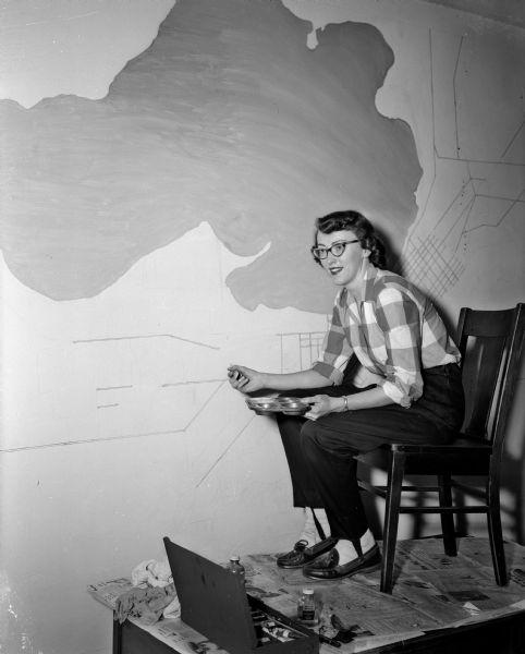Artist Joan Holm, daughter of John and Harriet Holm of 2318 Rugby Row, painting a mural map of the city of Madison on a wall in the business offices of Madison Newspapers, Inc., 115 South Carroll Street.