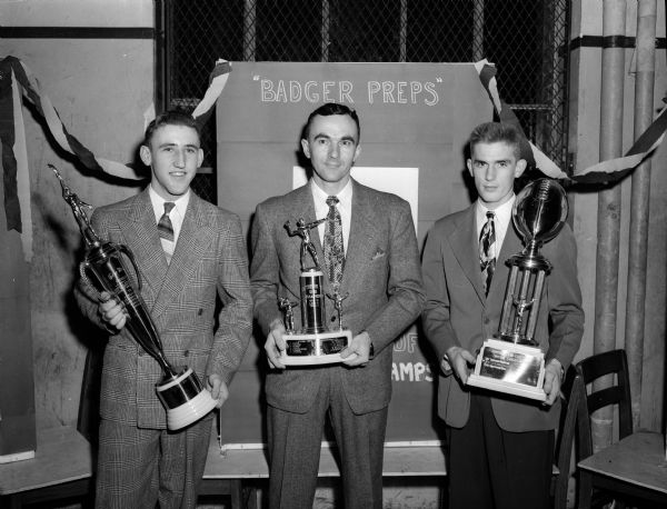 Three trophy winners from Wisconsin High posing for a group portrait with their trophies. Bob Spoentgen, left, was voted most valuable player. Coach Harold Metzen, center, is holding the trophy for the Southern 10 Conference title. Jerry Herling, right, was elected captain by his teammates after the season was over.