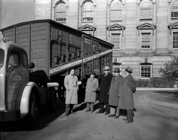 Five men, including State Historical Society Director, Clifford Lord at left, standing near a box car labeled "Gratitude Train" on a flat bed truck parked in front of the Wisconsin State Capitol building. The boxcar contains gifts to the people of Wisconsin from the people of France. Recipients of the articles were decided upon by the Governor's "Commission to Receive the Gratitude Train."