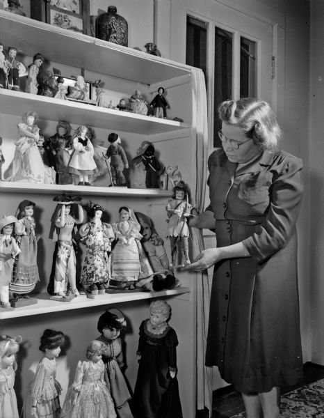 Mrs. Otto Koberle of Middleton is standing next to her bookcase of dolls. Mrs. Koberle has collected between 200 and 300 dolls that fill the living room of her modest farmhouse.