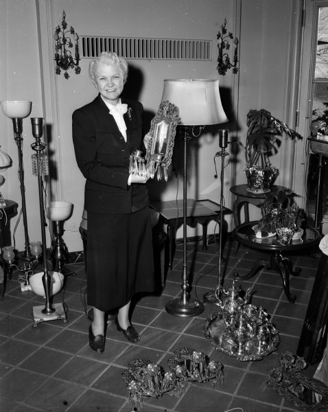 Wisconsin's First Lady, Mrs. Rennebohm, standing in the midst of furnishings that sixteen Rennebohm employees moved to the new executive residence at 101 Cambridge Road in Maple Bluff from the "old" mansion at 130 East Gorham Street in Madison.