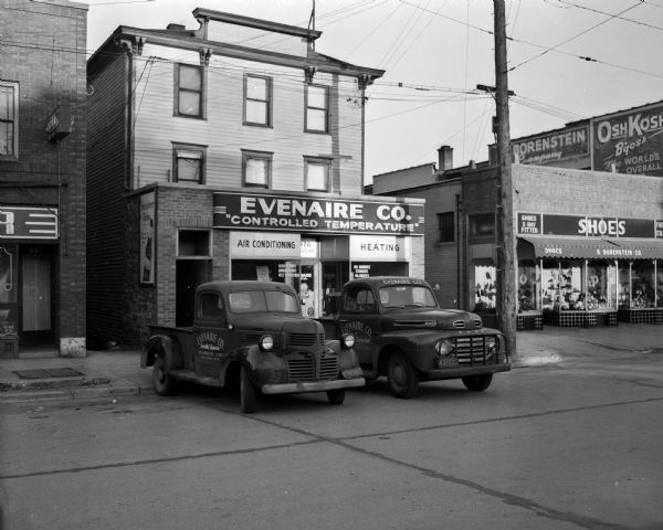 Two company trucks parked in front of the Evenaire Company "Controlled Temperature" building, located at 1976 Atwood Avenue. Photograph used in an advertisement for Heil natural gas furnaces.