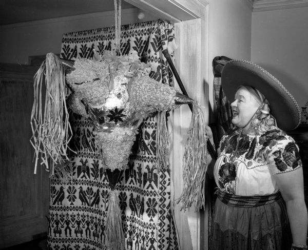 Mildred Holdhusen is shown striking a pinata at the Madison Woman's Club "Posada Mexicana" Christmas folk festival.