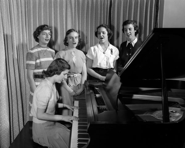 Some of the girls of the Blessed Sacrament Girls Choral group prepare for a cantata to be performed to raise money to purchase the grand piano in the picture. At the piano is Sheila Searls. Standing, left to right, are: Marcia Michel, Elizabeth Denu, Loretta Berkely, and Jean Tiedeman.