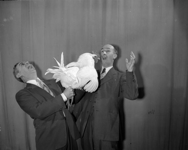 Two co-chairmen hold a chicken to be given as a special prize at the Nakoma 12th Night Party.  Donald Dohr, 4150 Cherokee Drive, stands at left, and Sidney Knope, 926 Waban Hill, stands beside him.