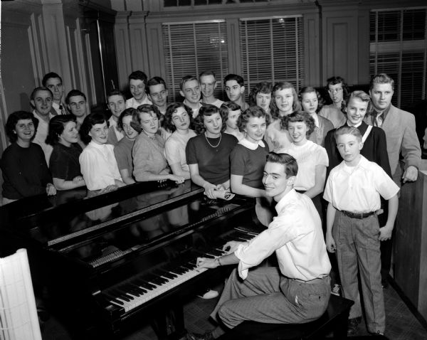27 teen singers stand behind a piano at the Madison YWCA. The group was formed by Don Voss (extreme right) with the cooperation of the East Side Youth Activities council. The pianist is Jim Peterson.