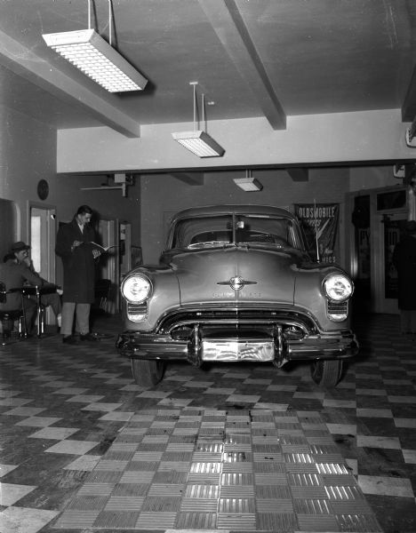 A new Oldsmobile car on display, probably in the showroom of Pyramid Motor Company Incorporated, 434 West Gilman Street, with a salesman and possible customer.