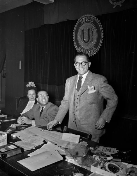 Standing is William Calvano, Milwaukee, national president of UNICO National, (Italian-American Service Organization - UNICO is the Italian word for unique). Sitting at left is Dorothy Matranga, chapter secretary and in the center is Joseph Bruno, chapter president. On the wall is displayed the UNICO National symbol.
