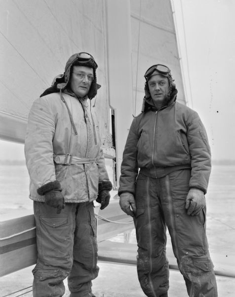Two Madison iceboat racers standing by their iceboat during the Hearst Trophy Race on Lake Monona. At left is Carl Bernard, skipper, with crewman, Norm Braith.