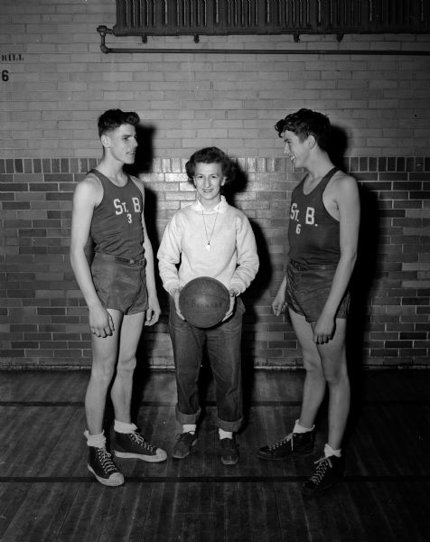 St. Bernard's Catholic School basketball coach, Marianne "Johnny" Zier, holds a basketball while standing between two of her star players, Ed Perkl (left) and Jim Joachim. Coach Zier was featured because women basketball coaches were unusual and the team was undefeated.