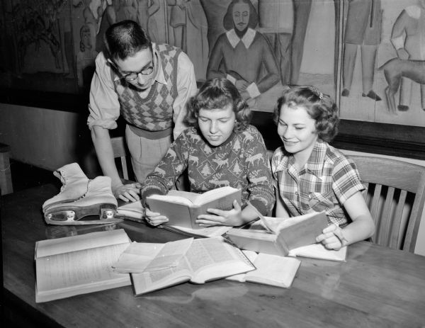 Three Central High School students gather at a table to study for final semester exams. A women's pair of ice skates are on the table. They are, from left, Bob Schwaratz, Betty Searle, and Shirley Morschhauser.
