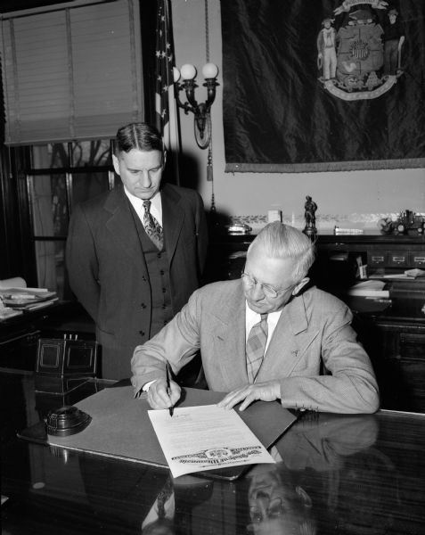 Wisconsin Governor Oscar Rennebohm signing a proclamation officially announcing the observance of Nation Brotherhood Week. With him is Wisconsin Supreme Court Justice Timothy Brown, general chairman of Brotherhood Week in Madison.