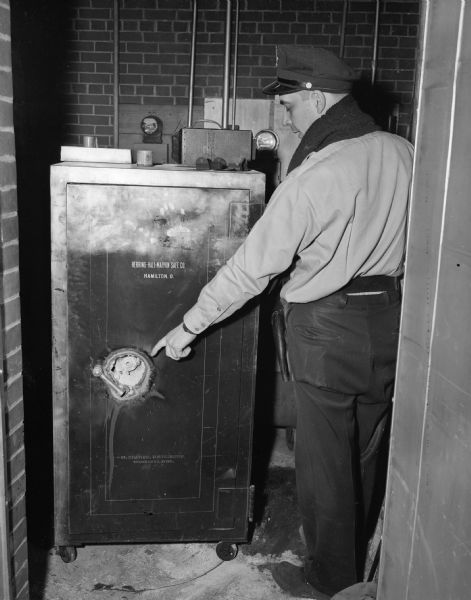 Police Investigator Ralph Nedderman is shown examining the torch-burned safe at the John Deere Farmers Implement Co., 110 N. Thornton Avenue. Two other locations were also robbed the same night.