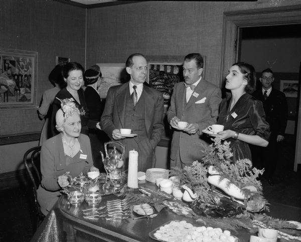 Madison Art Association sponsored a tea at the Madison Free Library in connection with the exhibit of the works of Madison artists.  
Mrs. Oscar (Mary) Rennebohm, Wisconsin's First Lady, is shown as she poured tea.  Gathered around the table are (left to right): Mrs. Bentley (Leonora) Courtenay, Wilbur D. Peat of Indianapolis, Indiana, who was the judge for the art exhibit, Colonel Bentley Courtenay, and Mrs. Frederick Carpenter.
