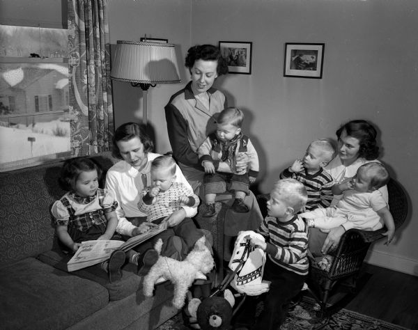 Members of a child study group of the University of Wisconsin Dames are shown engaged in recreation for children. Three members, shown with their children, are (left to right): Mrs. Lester (Elizabeth) Barnes, 919 W. Dayton Street, reads to Marianne Pond and her own baby son, Steven Barnes; Mrs. William L. (Peggy) Pond, 3630 Cross Street, with her young buckaroo, Jonathan; and Mrs. Arnold J.(Mary J.)Petersen, 3726 Gregory Street, with her three sons, Paul, Dana, and Jay.