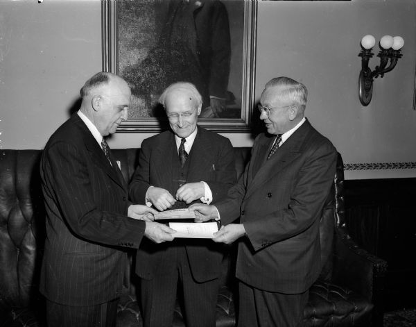 The historic governor's residence, 130 East Gilman Street, passed officially into University of Wisconsin hands. U.W. President Fred (left) hands a $60,000 purchase check to Governor Rennebohm (right) as Prof. William H. Kiekhofer (center), University economist and purchase advocate, looks on.