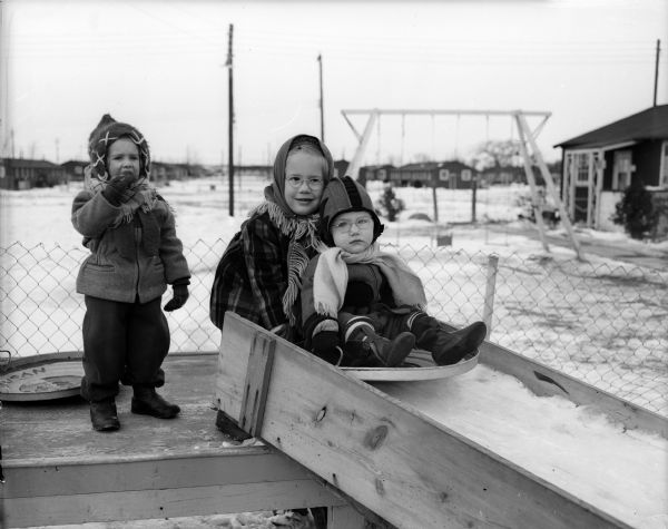 Children play on an ice slide created by two residents of the barracks apartments at Truax Field. A swing set is in the background.