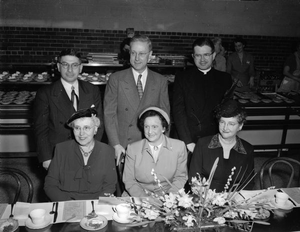 Six honored guests at the annual Founders' Day Banquet of the Madison Council of Parents and Teachers gather at a table for a group portrait. Seated, left to right, are: Mrs. William A. (Minnetta), past national PTA president; Mrs. E. (Flora) Steul, president of the Madison council; and Mrs. Edward J. (Helen) Samp, representing the Madison Board of Education. Standing, left to right, are: Rabbi Manfred Swarsensky; Dr. Carl Neupert, state health officer; and Rev. Mark Barron, chaplain of Edgewood high school.