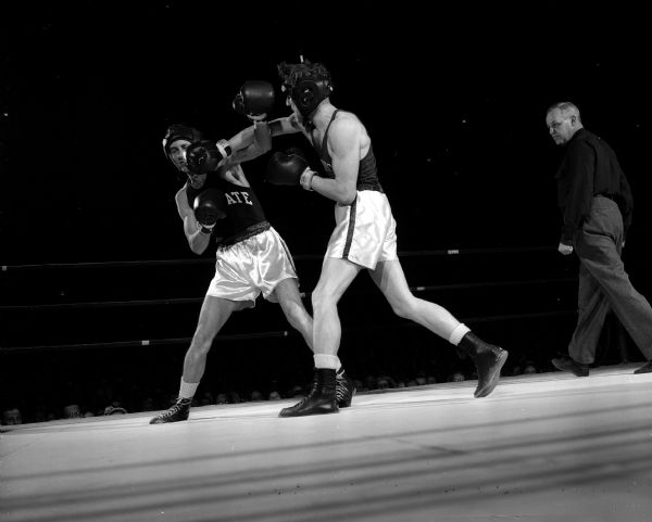 University of Wisconsin's Steve Gremban (right) delivers a right jab to the jaw of Penn State's John Hamby as a referee and audience are looking on.