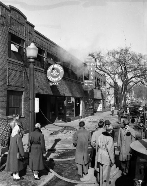 Spectators watch as black smoke pours from the burning second floor of the Pyramid Motor Company at 434 West Gilman Street after a gas tank explosion that shattered a downstairs window and rocked adjacent buildings. The explosion and fire injured seven employees.