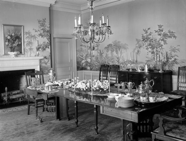 The dining room at the Wisconsin Governor's Residence with its scenic wallpaper is one of the loveliest rooms in the house. The rich antique blue of the rug sets the color scheme for the room and furniture that was brought from the old mansion. Table is decorated by the Who's New Club for a tea. Tall palladian windows provide a view toward Lake Mendota's brillant sunsets.