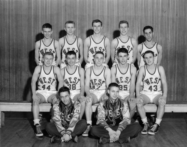 Group portrait of the West High School basketball team, dressed in uniform. Managers seated in front: George Fabian, left, and Jack Podell. Players seated, left to right: Jim Mahoney, Andy Ragatz, Jim Clapp, Bill Marshall, and Ed Sorenson. Standing, left to right:  Tom Mack, Evert Wallenfeldt, Owen Roberts, Jackie Mansfield, and Jim Namio.