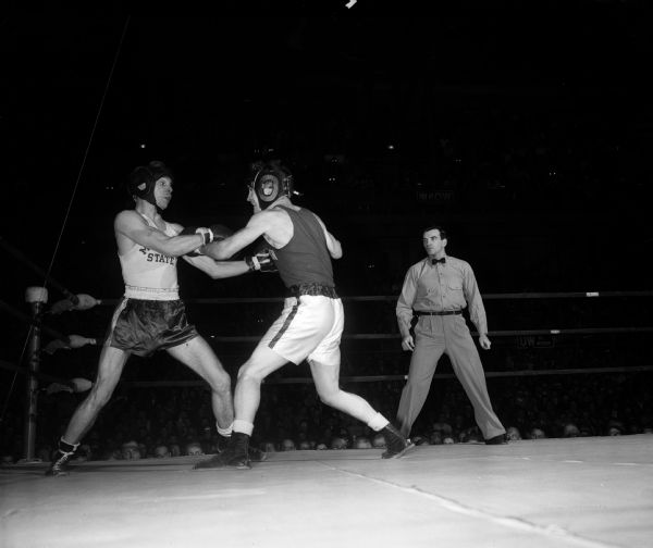 James "Red" Sreenan, 130 pounds, boxes with Henry Amos of Michigan State to a draw. The referee stands nearby in the ring and the audience is seated in the auditorium floor and upper deck in the background.
