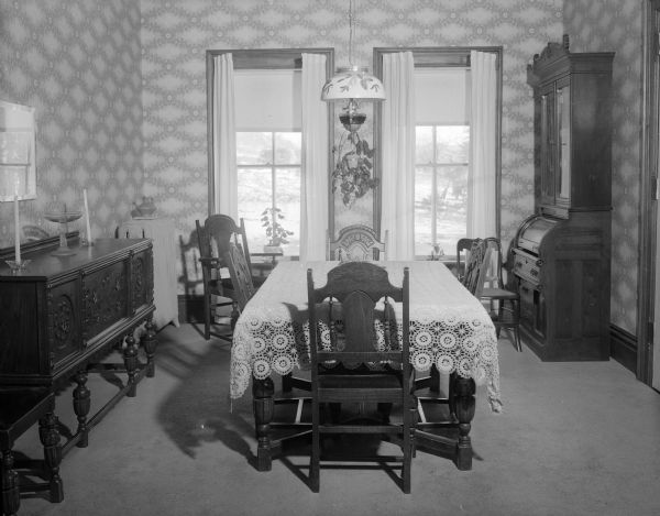 View of the furniture in the dining room of the home of Mr. and Mrs. H.D. Brainard. The home was formerly the 1878 "old Don Johnson farm" in Bear Valley which the Brainard's purchased after the last member of the Johnson family died and willed the farm to the Salvation Army. The dining room separates the houses' two living rooms and is furnished with family antiques. Mrs. Brainard's china collection is exhibited in the carved oak sideboard at right.