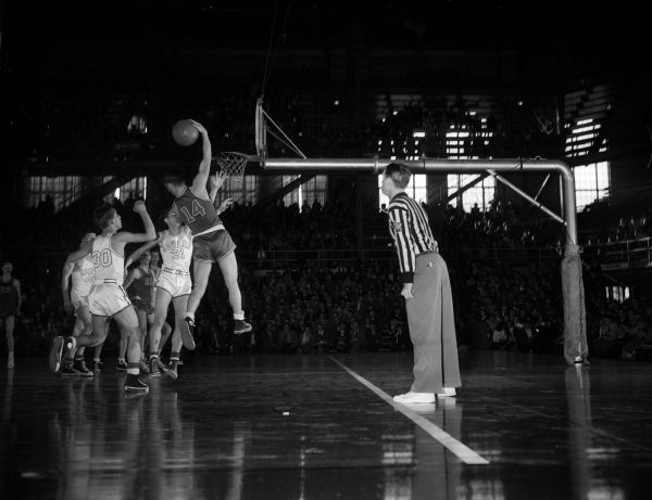 Action photograph of the consolation semi-final game of the state high school basketball tournament between Kohler and Onalaska. Sam Stuhr (#14) of Onalaska is grabbing a rebound in front of Kohler players Neil Mueller (#30), Lee Ebben (#31), and Bob Badura (#40). Earl Johnson (#21) is also playing.
