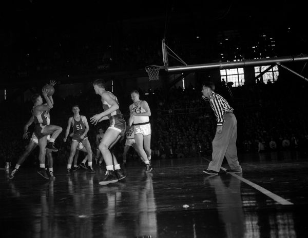 Action shot of the second consolation semi-final game of the state high school basketball tournament between Rhinelander and Wauwatosa. Rhinelander players are Bob Pohnl (#40 - shooting) and Dick Gilley (#51). Wauwatosa players are Bill Matthias (#43) and Jim Berner (#37).