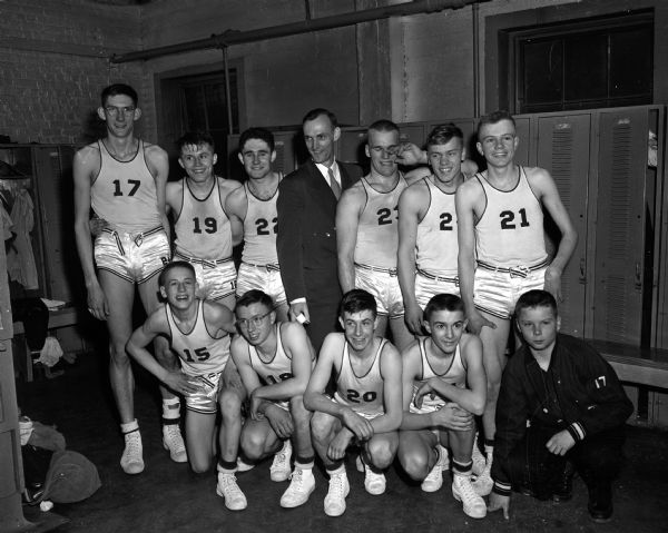 The state high school basketball champion team from St. Croix Falls poses in a locker room for a group portrait. They were the second-smallest town to win a state basketball title. Kneeling are: Dick D'Allier, Dick Hanson, John Beattie, Jerry Frank and manager Bob Berquist. Standing are: Paul Morrow, Larry Lundgren, John Edling, coach Don Snyder, Loren Kamish, Fred Horsmann, and Darrell Johnson.