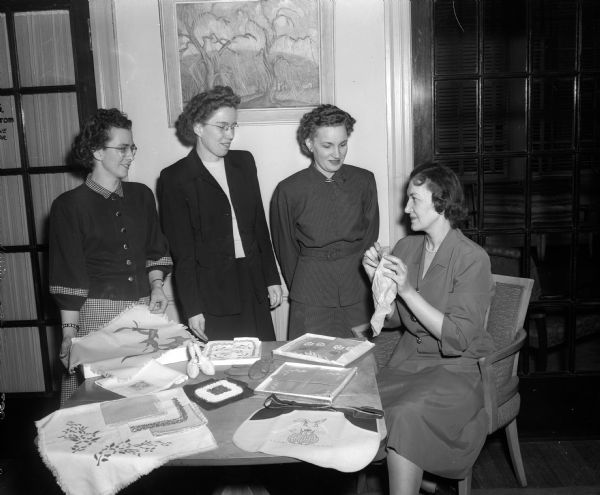 Four members of the YWCA Senior Business and Industrial Girls Club are standing and sitting around a table laden with items for a bazaar and bake sale. Left to right: Irene Holz, 2922 Arbor Drive; June Rose, 1013 Colby Street; Lorinda Fralick, 844 Prospect Place; and Ruth Kitzrow, 121 East Johnson Street, club president.