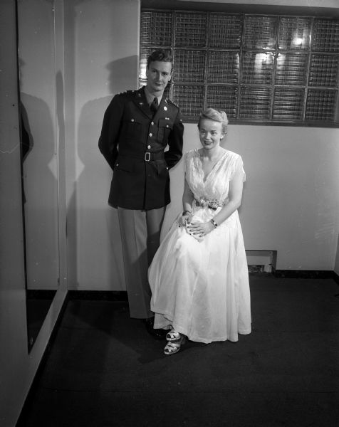 Richard McNall of Janesville, member of Alpha Gamma Rho fraternity and king of the University of Wisconsin Military Ball, standing beside queen Mary Olber of La Crosse, member of Kappa Alpha Theta sorority. McNall is wearing military uniform, and Olber is wearing a formal dress.