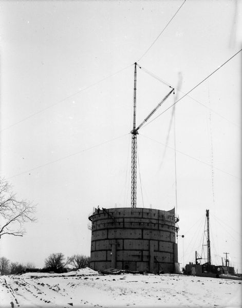 A large steel cylinder-shaped water reservoir stands above a drilled well with a tall construction crane behind it. The well under construction is Unit #9 at 4724 Spaanem Avenue in the Town of Blooming Grove (currently in the city of Madison).