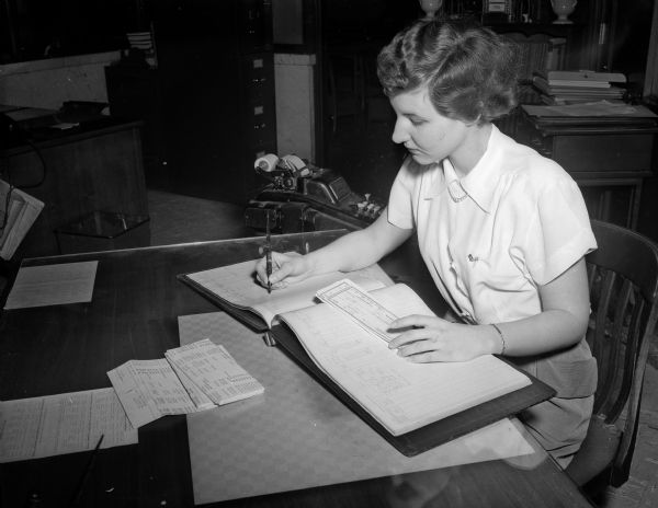 A female bookkeeping student works on a ledger at the Groves-Barnhart School, 502 State Street. The school trains secretaries, stenographers, bookkeepers, office clerks, and junior executives.