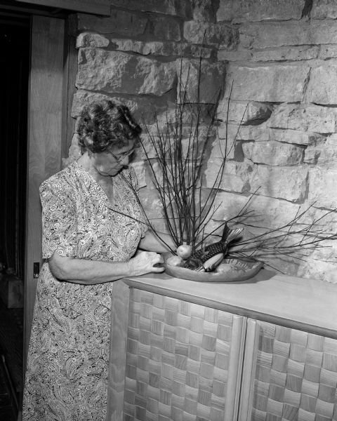 Caroline Peterson, noted flower arrangement artist from Hawaii, stands beside a floral arrangement on a wooden buffet.  The photograph was probably taken at the home of her friends Robert O. and June D. McLean.