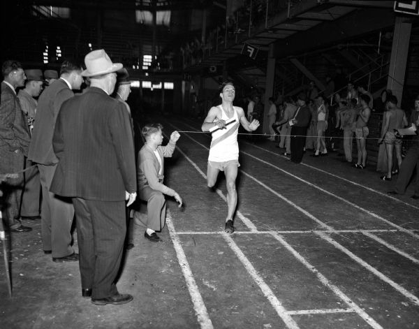 A runner breaks the tape at the finsih line. Image taken inside the University of Wisconsin-Madison Field House during the West High School relays.