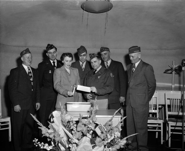 Mrs. Frieda Abrahams, president of the VFW woman's auxiliary, holds a candle to the mortgage held by C.L. Skinner, post commander. The ceremony was for the burning of the five-year-mortgage of the Lieut. Marion C. Cranefield Post Number 1318. Looking on, left to right, are: Albert Nonn, C.A. Lewis, Reynold Abrahams, A.J. Taff, and Earl Soper.