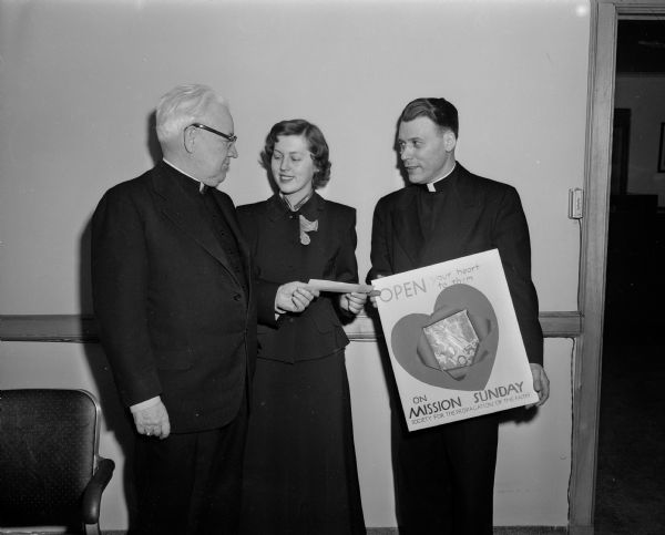 Bishop William P. O'Connor (left) presents a check to Marcia Pilon, an Edgewood College freshman, for her prize-winning poster for the Society for the Propagation of the Faith to promote Mission Sunday, the fourth Sunday in October. Her poster will be submitted to the national society in New York. Looking on and holding the poster is the Reverend Edward B. Auchter, pastor of St. Mary's of the Lake parish in Westport and director of the society.