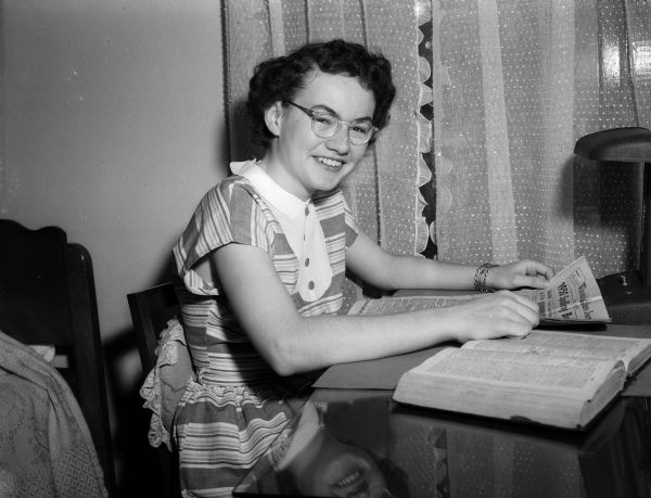 Barbara North of 1003 Jenifer Street, the spelling champion of the Madison Lutheran School, sits at a desk while reading a newspaper. A dictionary lies open beside her.
