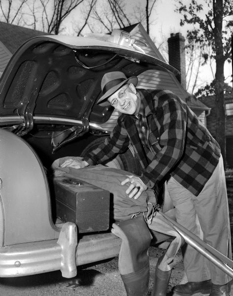 Fisherman Roy "Chubby" Goodlad is shown at the open trunk of his car loading in fishing poles, a tackle box, and hip waders in preparation for the opening day of fishing season.
