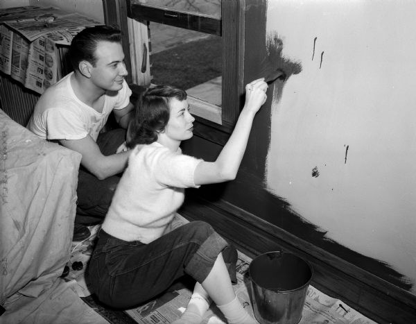 Newlyweds George and Lorna Holmes decorate their first apartment at 1028 Erin Street.  Lorna is painting a living room wall as George is looking on.