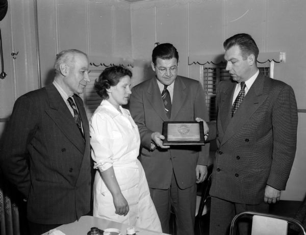 Homer Vorel (right), safety engineer for Employer's Mutual Insurance Company presents an award to Victor Gruendler, safety director for the Madison-Kipp Corporation at 201-231 Waubesa Street, for an outstanding industrial safety record during 1949. Witnessing the presentation are A.J. Ahrensmeyer, Kipp mechanical superintendent, and Mrs. Freda Bollman, industrial nurse, both standing at left.