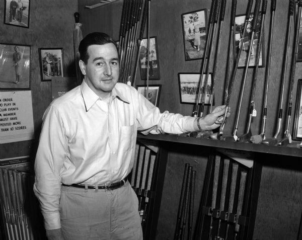 Dick Jackson, assistant manager to "Cully" Schlict at Blackhawk Country Club, stands beside rows of golf clubs stored in the clubhouse.