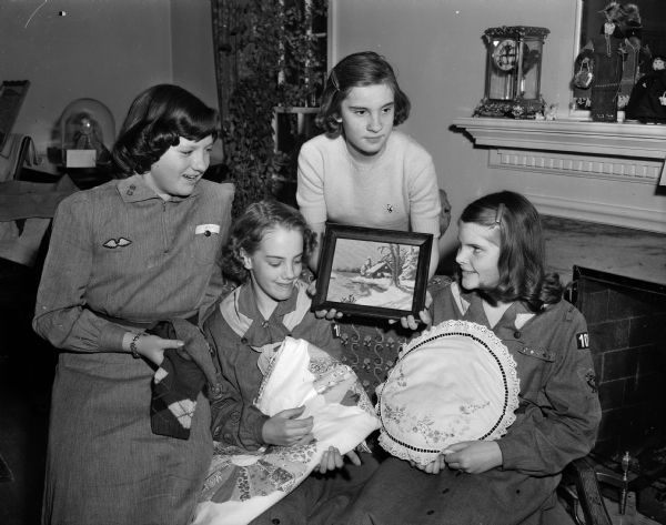 Members of Nakoma Girl Scout Troop 107 displaying their needlework projects. Shown left to right are Katy Grimmer, 4018 Council Crest, holding the mittens and argyle socks she knit; Virginia Pochmann, 3930 Manitou Way, holding the quilt she made herself; Barbara Vogel, 737 Oneida Place, holding her framed needlepoint winter landscape, and Jeanne Larson, 3914 Nakoma Road, with her cross-stitch and embroidered pillow.