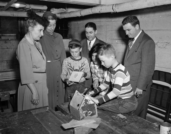 Members of the Community Chest budget committee are shown craft work done by three boys at Neighborhood House. Members of the committee, left to right, are: Mrs. P.H. (Celestine) Hyland, Mrs. Russell O. (Harriet) Morris, John Sonderegger, and John Brickhouse. The boys showing their crafts are, left to right: Anthony Fiore, Peter Cerniglia, and Delbert Wagner.