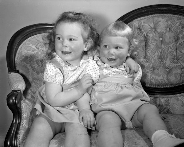 Joan Carol, 3 years, and Ruth Ann, 15 months, daughters of Lieut. Col. Glenn and Mrs. Stell of 5-D University Houses, sitting on a couch for a portrait. The photograph was one of a collection of baby photos on the Society Page for observation of National Baby Week.