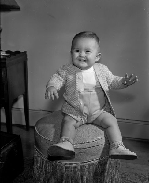 Thomas W., the nine-month-old son of Kenneth and Mary Conlin of 208 West Gorham Street, posing for a portrait while sitting on an ottoman. The photograph was one of a collection of baby photos on the Society Page for observation of National Baby Week.