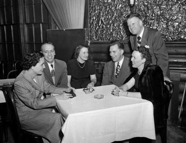 Three couples who attended the spring dance party of the Who's New Club at the Club Chanticleer are sitting around a table. The couples, left to right, are: Mr. and Mrs. Harry Brown, Mr. and Mrs. Harmon Smith, and Mr. and Mrs. George Armour. An ashtray and a pair of novelty eyeglasses are sitting on the table.